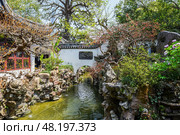 Shanghai, China - 1 April 2025: Scenic view of a traditional Chinese garden with pond, rock formations, and trees in full bloom inside the historic Yu Garden. Редакционное фото, фотограф Татьяна Терехина / Фотобанк Лори