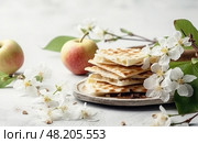 Jewish matzo bread with flowering twigs and apples on a white background. The concept of the Passover holiday. Стоковое AI-изображение, AI-художник Данила Большаков / Фотобанк Лори