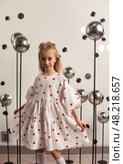 In a creative studio filled with playful decor, a 6-year-old girl gracefully twirls while wearing a charming white dress adorned with red hearts. Стоковое фото, фотограф Aleksandr Golubev / Фотобанк Лори