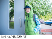 мальчик открывает дверь в подъезд весной, ребенок возвращается из школы весной домой. Стоковое фото, фотограф Яна Проничева / Фотобанк Лори