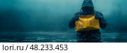 Amidst pouring rain, an individual in a hooded jacket clutches a yellow envelope, standing in water on a dreary day. Стоковое AI-изображение, AI-художник Данила Большаков / Фотобанк Лори