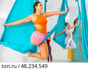 Young women making antigravity yoga exercises with group of people. Стоковое фото, фотограф Яков Филимонов / Фотобанк Лори