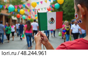 A close-up of a child's hands holding a small Mexican flag, their face painted with traditional designs. The scene is set in a bright street. Стоковое AI-видео, аниматор Sergey Grishin / Фотобанк Лори