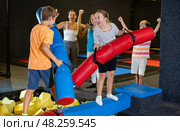 Preteen girl fighting by pugil stick with boy on inflatable beam. Стоковое фото, фотограф Яков Филимонов / Фотобанк Лори