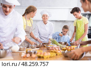 During cooking lesson, female cook tells children about culinary rules, guy assistant helps child. Стоковое фото, фотограф Яков Филимонов / Фотобанк Лори