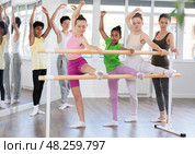 Teenage girls doing leg stretching exercise holding by ballet barre during dance courses. Стоковое фото, фотограф Яков Филимонов / Фотобанк Лори