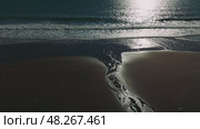Soft sunset light illuminating dark sandy coastline, golden reflections rippling across wet shore with gentle waves washing over serene oceanfront landscape. Стоковое видео, видеограф ILIA GOROKHOV / Фотобанк Лори