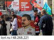 Мужчина держит плакат с потертом Иосифа Сталина на фоне праздничных баннеров приуроченных к празднованию 80-летия Победы в Великой Отечественной войне, Россия. Редакционное фото, фотограф Николай Винокуров / Фотобанк Лори