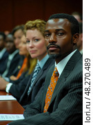 A man in a striped suit and bright tie focuses intently as part of a diverse group attending a courtroom session in a bustling city environment. Стоковое AI-изображение, AI-художник Данила Большаков / Фотобанк Лори