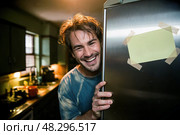 Man looks out from behind a refrigerator with a yellow sticker on it. Стоковое AI-изображение, AI-художник Дмитрий Киселёв / Фотобанк Лори