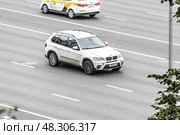 White BMW X5 car is moving on city street. Automobile driving fast along urban speedway with blurred background. Редакционное фото, фотограф Константин Григорьев / Фотобанк Лори