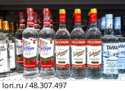 Столичная и другие русские водки продаются на полке в супермаркете. Бутилированные алкогольные напитки и крепкие напитки (2023 год). Редакционное фото, фотограф FotograFF / Фотобанк Лори