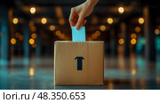 A hand places a ballot into a cardboard box labeled with a shirt icon, surrounded by soft evening lighting in a voting area. Стоковое AI-изображение, AI-художник Данила Большаков / Фотобанк Лори