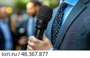 A professionally dressed person holds a microphone, preparing to address a gathering of listeners in an outdoor setting on a bright day. Стоковое AI-изображение, AI-художник Данила Большаков / Фотобанк Лори