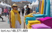 Elegant woman browsing colorful textiles at outdoor market. Стоковое AI-видео, аниматор Юрий Поздников / Фотобанк Лори
