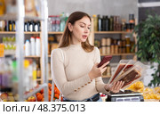 In trading floor of minimarket, girl buyer inspects hamon, scan QR code on product label. Стоковое фото, фотограф Яков Филимонов / Фотобанк Лори