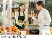 Female seller hold out basket with hanging sweets and invites girl buyer to familiarize with product. Стоковое фото, фотограф Яков Филимонов / Фотобанк Лори