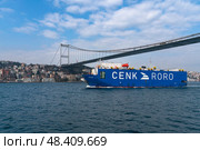 Istanbul, Turkey, 02.25.2023: Cargo ship CENK RORO passing under the Sultan Mehmed Fatih Bridge in the waters of the Bosphorus on a sunny day. Редакционное фото, фотограф Ula Ulachka / Фотобанк Лори