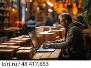 Mature man wearing a brown hoodie is sitting at a table with a laptop. Table is surrounded by many boxes. Стоковое AI-изображение, AI-художник Данила Большаков / Фотобанк Лори