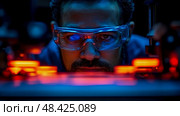 A technician, wearing protective goggles, closely examines small parts illuminated by vibrant red lights in a dim laboratory setting. Стоковое AI-изображение, AI-художник Данила Большаков / Фотобанк Лори