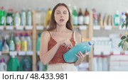 Pleased young girl in summer clothes reviewing washing detergents to buy in supermarket. Стоковое видео, видеограф Яков Филимонов / Фотобанк Лори