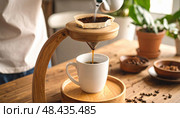 A handcrafted wooden coffee dripper pours into a ceramic mug showcasing slow living, artisanal design, eco-conscious routines, and modern morning rituals. Стоковое AI-изображение, AI-художник Igor Tichonow / Фотобанк Лори