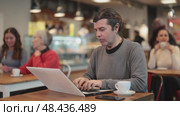 Middle-aged man sitting at table, using laptop and enjoing cup of tea in coffee house. Modern lifestyle concept. Стоковое видео, видеограф Яков Филимонов / Фотобанк Лори