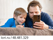 Father and son little boy laughing and using phone. They watching funny videos together, playing games on smartphone. Concept technology, smart phone addicted. Fun weekend activity. Modern fatherhood. Стоковое фото, фотограф Марина Демидюк / Фотобанк Лори