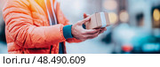 Swift Package Delivery: A man in orange jacket handoff box against city backdrop, perfect for showcasing logistics. Стоковое AI-изображение, AI-художник Данила Большаков / Фотобанк Лори