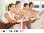 Dedicated young girls ballet dancer performing leg stretch at barre with concentration and grace in choreography studio during group rehearsal. Стоковое фото, фотограф Яков Филимонов / Фотобанк Лори