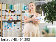 Tired pregnant woman stands with armful of purchases of cosmetics and drugs in pharmacy. Стоковое фото, фотограф Яков Филимонов / Фотобанк Лори