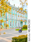 Russia, St. Petersburg, 10 May 2025: the incredibly picturesque facade of the Winter Palace through the branches of trees on a clear spring day, actors in tsarist outfits, the heritage of Russia. Редакционное фото, фотограф Vladimir Drozdin / Фотобанк Лори