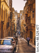VALLETTA, MALTA - NOVEMBER 12, 2018 - Hilly ancient streets view with colourful balconies, people and cars in the medieval city. Редакционное фото, фотограф Сергей Богомяко / Фотобанк Лори