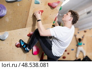 Teenage boy climbs steep artificial wall in sports complex and trains endurance. Стоковое фото, фотограф Яков Филимонов / Фотобанк Лори