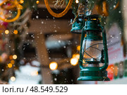 A beautiful antique kerosene lamp made of green decorative metal hanging on a snowy fir tree. A postcard for design. The concept of preparation and decoration. New Year's card 2026. Стоковое фото, фотограф Photojuli / Фотобанк Лори