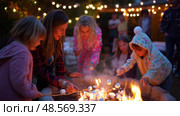 Family gathers around bonfire to roast marshmallows while enjoying a cozy evening outdoors. Стоковое AI-изображение, AI-художник Сергей Толмачёв / Фотобанк Лори