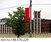 Красный флаг и старые заводские помещения, фабричный городок в городе Раменское, Московская область. Пасмурный день (2019 год). Редакционное фото, фотограф Александр Кузнецов / Фотобанк Лори