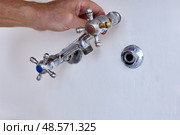 Removing old wall mounted kitchen faucet with two cross handles from hidden pipe in concrete wall, spout already detached, visible hand holding fixture. Стоковое фото, фотограф Владимир Григорьев / Фотобанк Лори