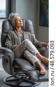 Senior woman relaxing in recliner chair at home. Стоковое AI-изображение, AI-художник Юрий Поздников / Фотобанк Лори