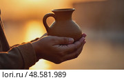 A child's small hands holding a clay water jug, symbolizing the thirst of Imam Hussain family, under the fading light of sunset. Стоковое AI-видео, аниматор Sergey Grishin / Фотобанк Лори
