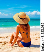 A beautiful girl in a swimsuit and a wide-brimmed straw hat on the beach on a sunny day looks at the surf. Стоковое AI-изображение, AI-художник Сергей Елизарьев / Фотобанк Лори