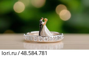 Miniature couple on wedding ring captures love and celebration indoors. Миниатюрная пара с обручальным кольцом. Стоковое AI-изображение, AI-художник Katsiaryna Repich / Фотобанк Лори