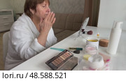 A beautiful senior woman is sitting at home and doing her make-up morning routine. Senior woman putting blush on her face. Стоковое видео, видеограф Ирина Старикова / Фотобанк Лори