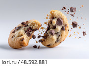Perfectly baked chocolate chip cookie breaking apart with flying pieces. Идеально испеченное шоколадное печенье разлетается на кусочки. Стоковое AI-изображение, AI-художник Katsiaryna Repich / Фотобанк Лори