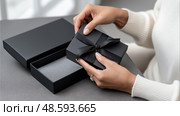 Top view of luxury unboxing scene with hands opening matte black packaging.  Роскошная сцена распаковки с руками, открывающими матовую черную упаковку. Стоковое AI-изображение, AI-художник Katsiaryna Repich / Фотобанк Лори