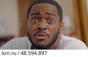 A man displays a shocked expression while indoors, conveying disbelief and confusion during a casual moment at home. Стоковое AI-изображение, AI-художник Данила Большаков / Фотобанк Лори