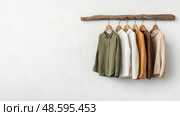 Stylish linen shirts and cotton trousers displayed on a wooden hanger. Стильные льняные рубашки и хлопковые брюки на деревянной вешалке. Стоковое AI-изображение, AI-художник Katsiaryna Repich / Фотобанк Лори