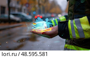 Concept: Futuristic Rescue; Firefighter holding augmented reality interface in palm, showing rescue operation data, for use in emergency response. Стоковое AI-изображение, AI-художник Данила Большаков / Фотобанк Лори