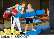 Tween girl fighting by pugil stick with female friend on inflatable beam. Стоковое фото, фотограф Яков Филимонов / Фотобанк Лори