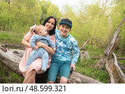 Семейное фото детей с матерью на природе. Мать и двое сыновей сидят на бревне в парке. Стоковое фото, фотограф Яна Проничева / Фотобанк Лори
